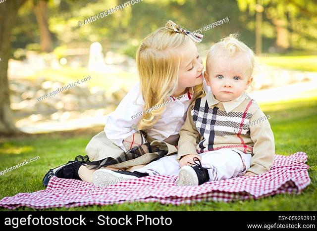Sweet Little Girl Kisses Her Baby Brother on His Cheek Outdoors at the Park.