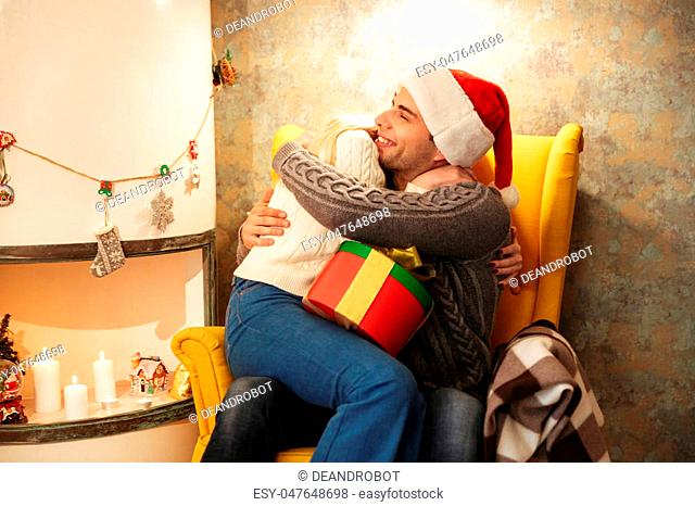 Happy couple hugging each other after gift exchange while sitting decorated room