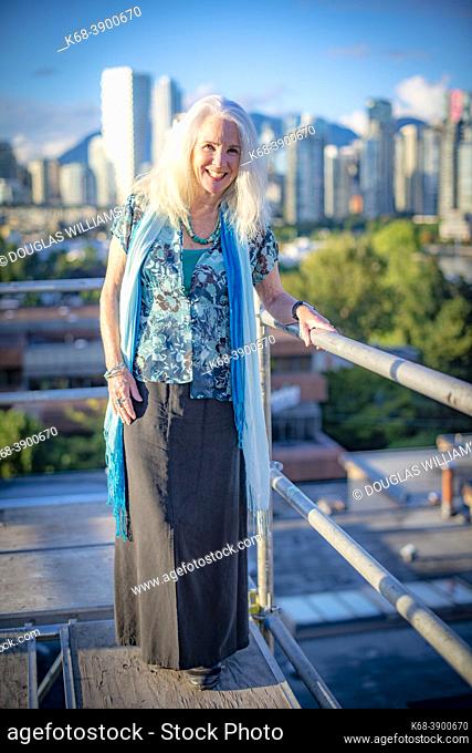 A woman, 70, in a portrait on a scaffold overlooking downtown Vancouver, BC, Canada