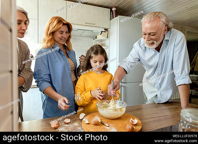 Three-generation family preparing dough for bread in kitchen