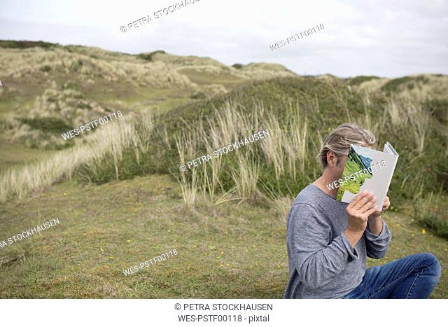 Man reading story book in the dunes, covering his face
