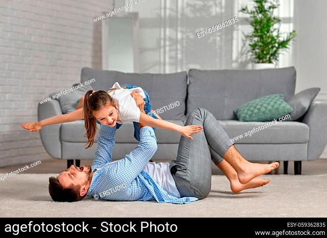 handsome father lying on carpet floor and lifting excited smiling little child girl at home