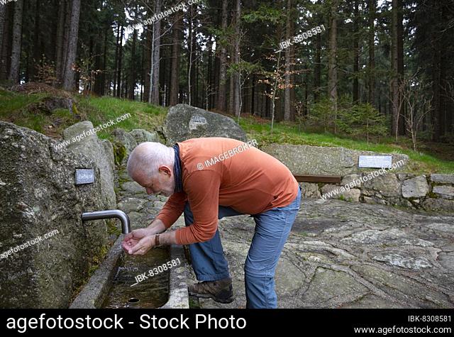 Hiker refreshes himself at the spring water fountain at the 1000 m square, Sternstein circular trail, Bad Leonfelden, Mühlviertel region, Upper Austria, Austria