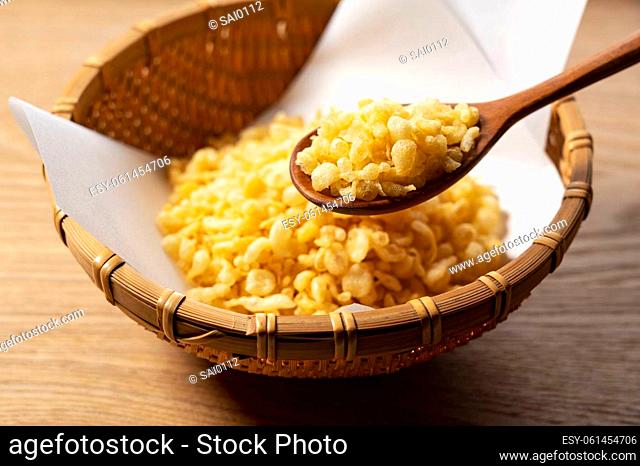 Tenkasu served in a colander placed on a wooden background with a wooden spoon. Image of Japanese food