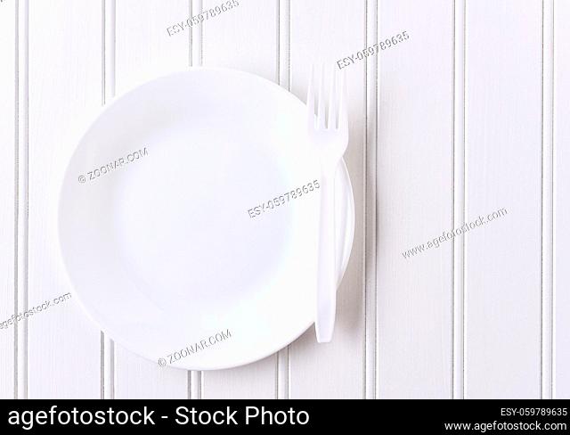 Top view of a white plate and white plastic fork on a white beadboard surface. Horizontal format with copy space