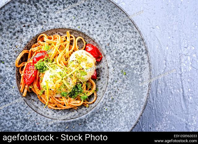 Modern design traditional fried scallops with tomatoes, broccoli pesto and Italian spaghetti pasta served as close-up on a Nordic design plate with copy space...