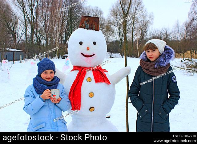 Two sisters play near snowman in winter day. Children make snowman. Two sisters make snowman in winter day