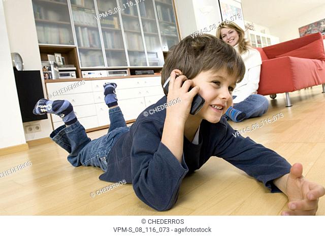 Side profile of a boy using a mobile phone with his mother sitting beside him