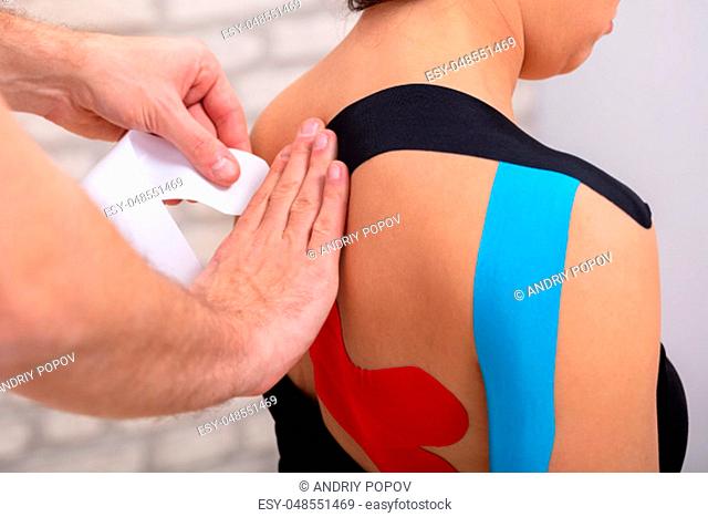 Close-up Of Man Hand's Applying Red Physio Tape On Woman's Back