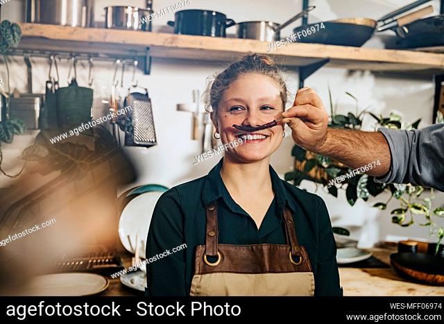 Chef making mustache of dry chili to colleague while standing in kitchen