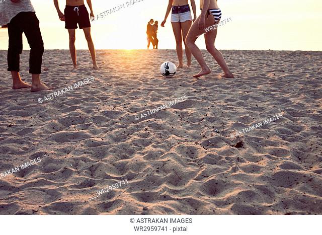 Young men, young woman and teenage girl (16-17) playing soccer on sand at sunset