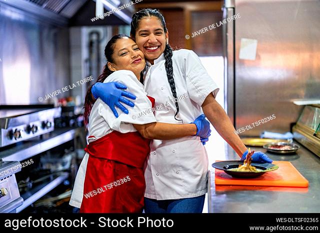 Happy kitchen trainees embracing each other in restaurant