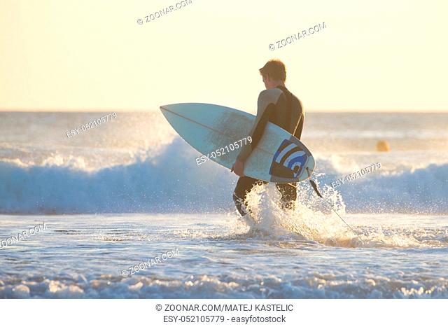 Silhouette of male surfer on the beach with the surfboard in sunset. Vertical composition