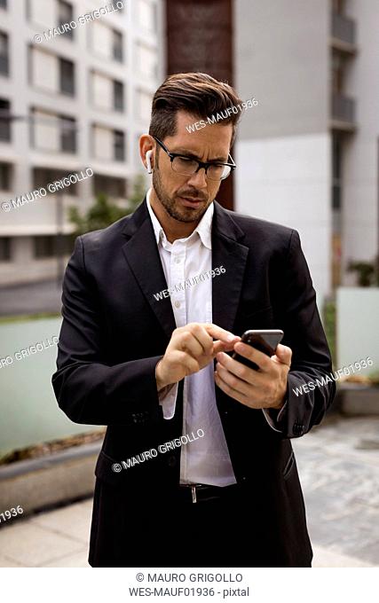Businessman with earbuds in the city checking cell phone