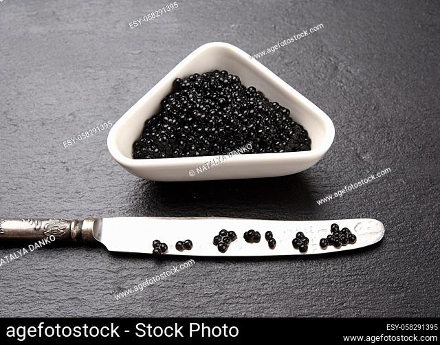 black grainy caviar of paddlefish fish in a white ceramic bowl, black background, top view