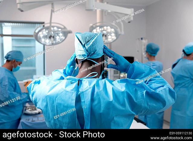 Mixed race doctors wearing face masks and surgical overalls standing in operating theatre