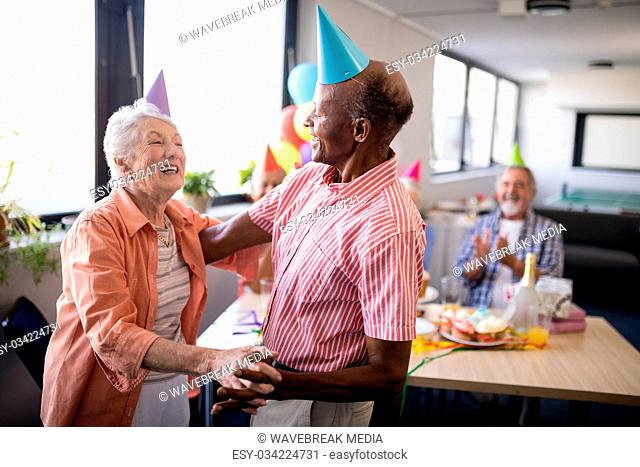 Senior couple wearing party hats dancing at birthday party