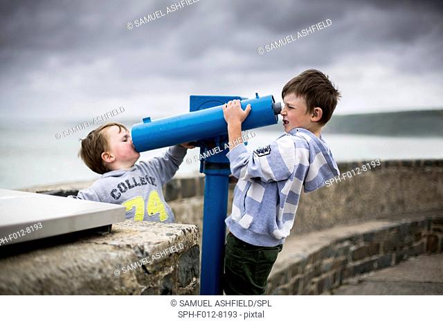 Two boys using coin operated telescopes at the seaside