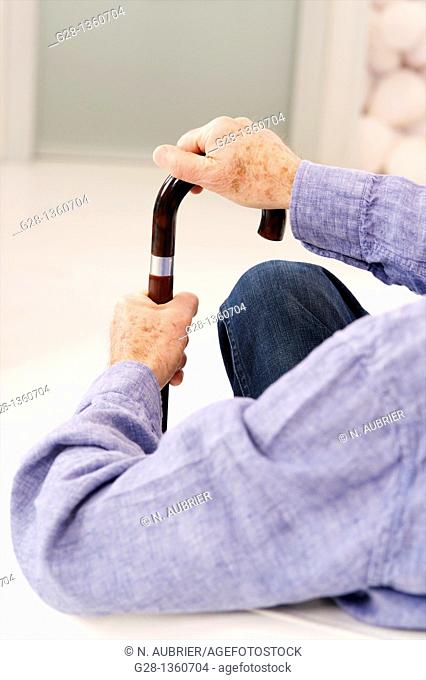 Senior mandetail seen from behind waiting with his hand on a crutch in a clinic waiting room or medical center