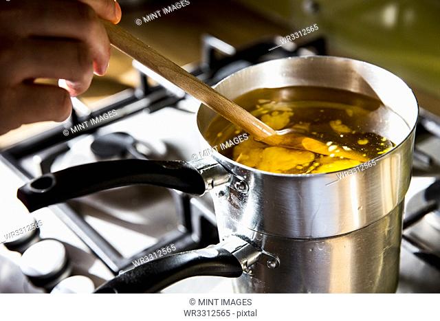 High angle close up of person melting wax for candles in saucepan on stove