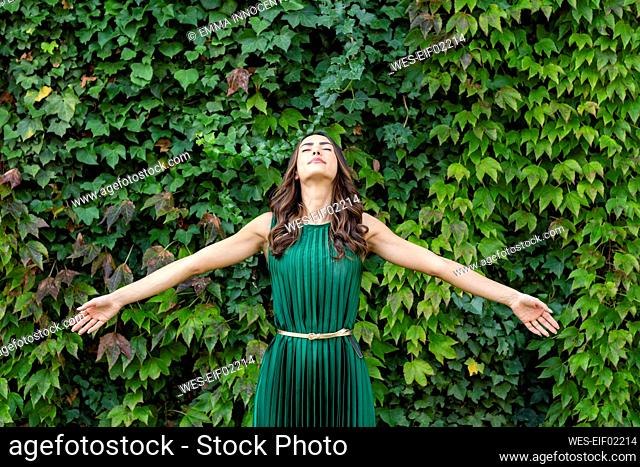 Carefree woman with arms outstretched in front of green ivy plants