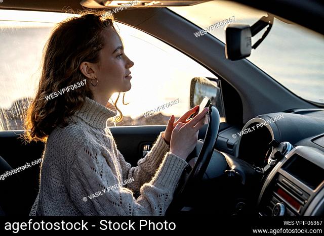 Smiling young woman with smart phone sitting in car