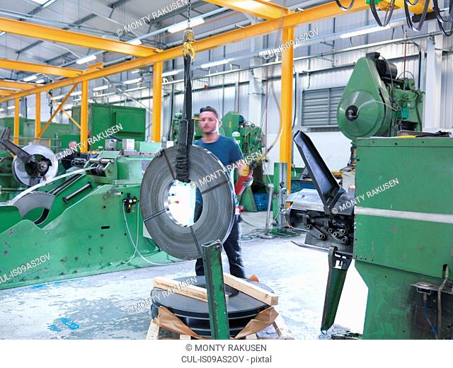 Worker loading rolls of metal into stamping machine in engineering factory