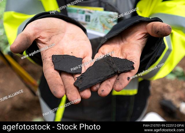 01 July 2021, Baden-Wuerttemberg, Balingen: An employee of the Landesamt für Denkmalpfelge shows unburned oil shale in a former slate oil pile