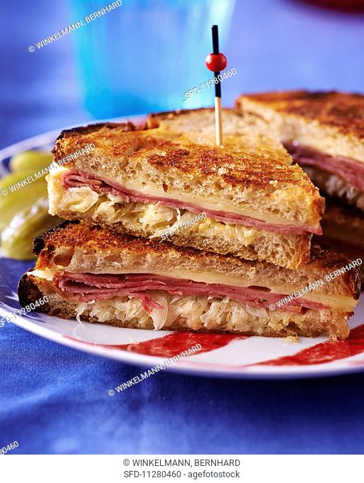 A toasted sandwich with pastrami, cheese and sauerkraut