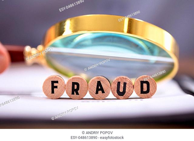 Close-up Of Magnifying Glass Over The Fraud Word Block