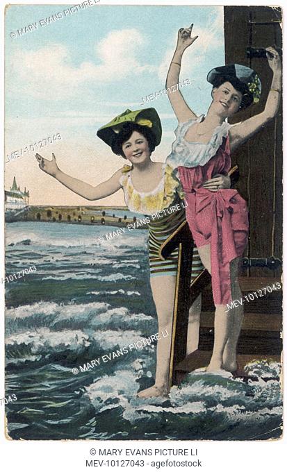 Two bathers in fancy swimsuits and hats pose theatrically on the steps of their bathing hut