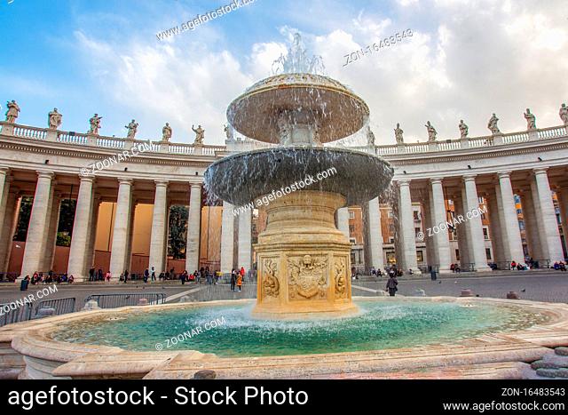 Fountain del Bernini in St. Peter's Square Vatican . Bright Italian sun (noon) Unrecognizable people are resting (sitting) under the colonnade