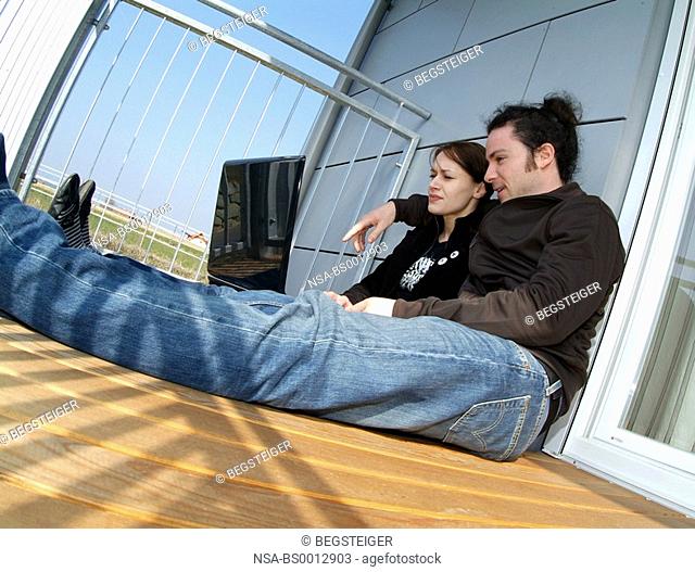 young couple on balcony using laptop