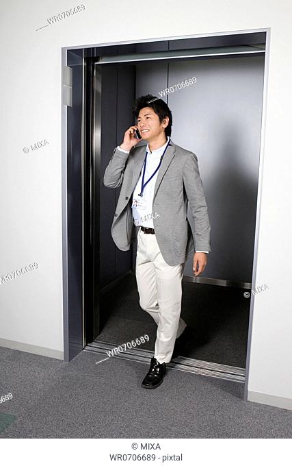 Businessman talking on smartphone and walking at elevator hall