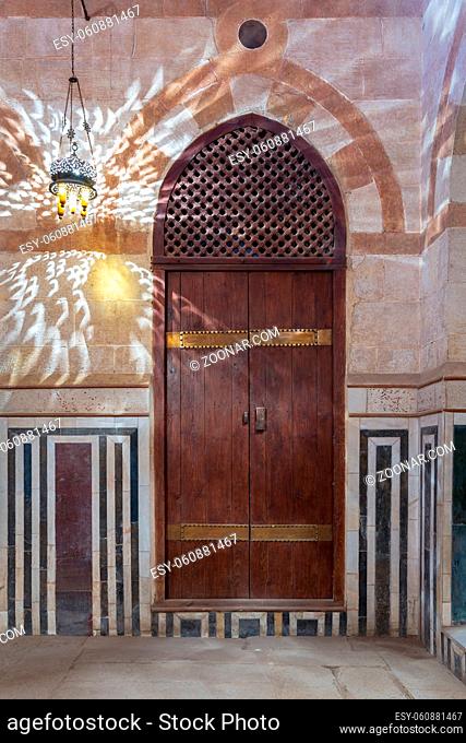 Wooden arched door on stone wall decorated with marble panels and lantern shadows on the wall, Khayer Bek Mausoleum, Darb Al-Ahmar district, Old Cairo, Egypt