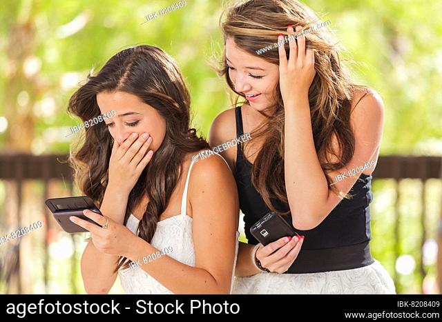 Two expressive mixed-race girlfriends using their smart cell phones outdoors
