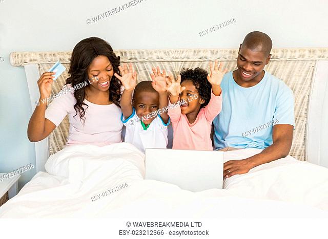 Happy family shopping online with laptop on bed
