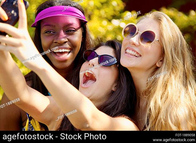 Happy teenage girl friends with sunglasses taking selfie