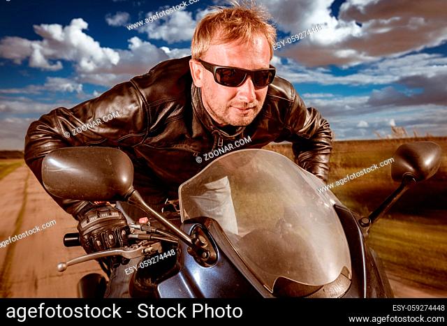 Biker in sunglasses and leather jacket racing on the road