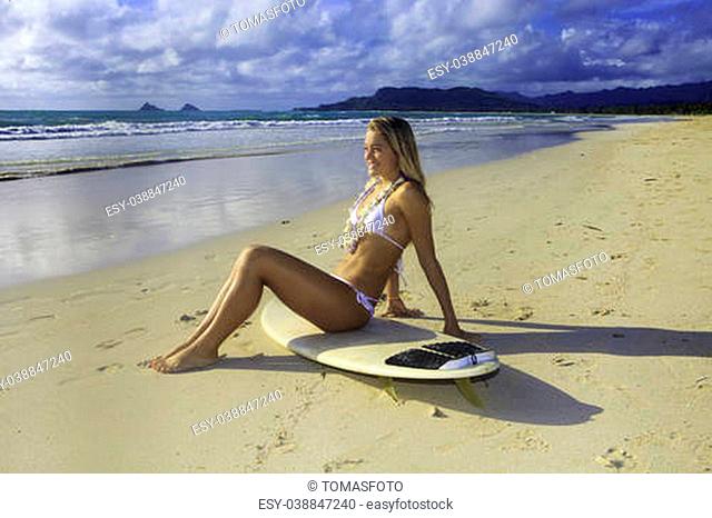 teenage girl in white bikini and flower lei with her surfboard at Kailua beach