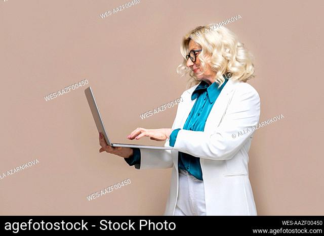 Senior businesswoman using laptop against colored background