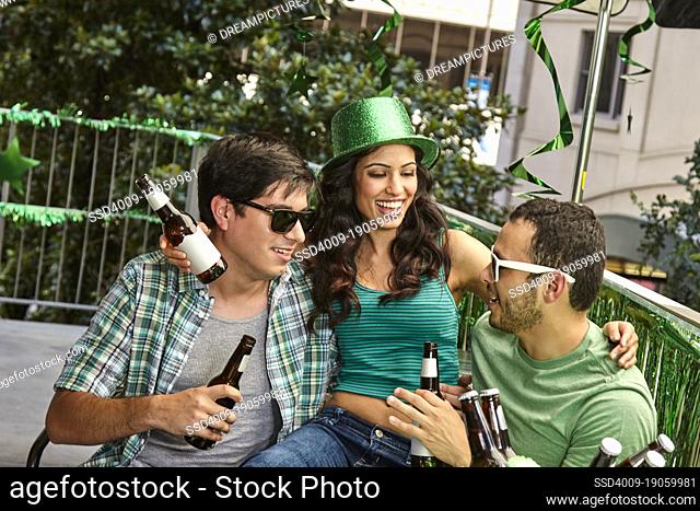 Woman sitting on laps on friends while celebrating St. Patrick's day outside drinking beer