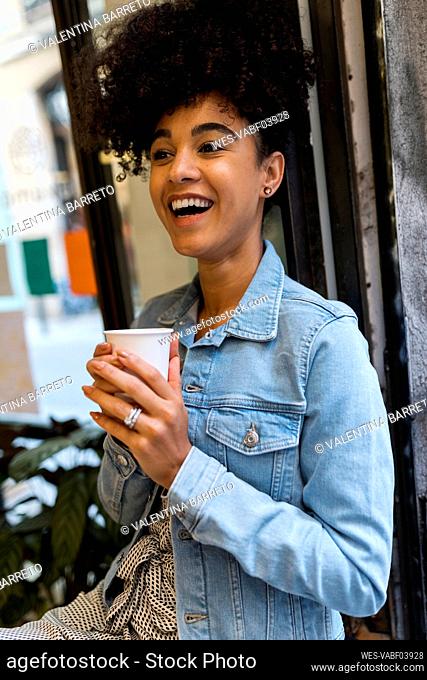 Smiling woman drinking coffee while sitting by window at cafe