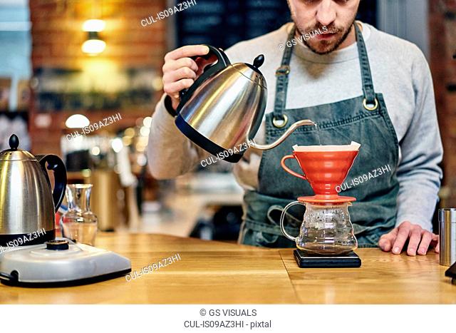 Barista pouring boiling water into coffee filter at coffee shop