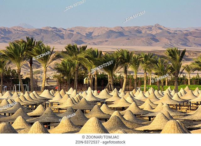 Mountains in a desert with beach and parasols in the foreground