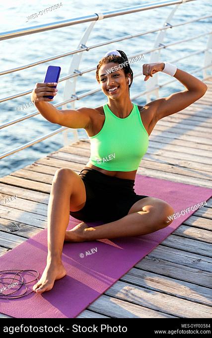 Happy woman flexing muscle while talking selfie through mobile phone