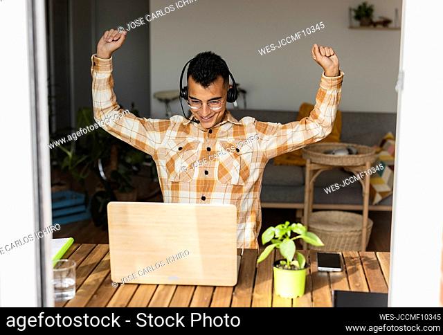 Freelancer with arms raised doing video call on laptop at home office