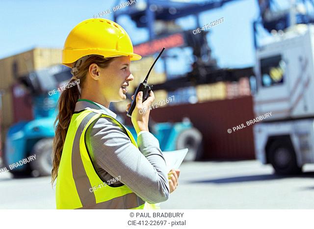 Businesswoman using walkie-talkie near cargo containers and trucks