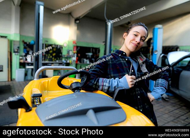 Female mechanic with screwdriver leaning on toy car at workshop