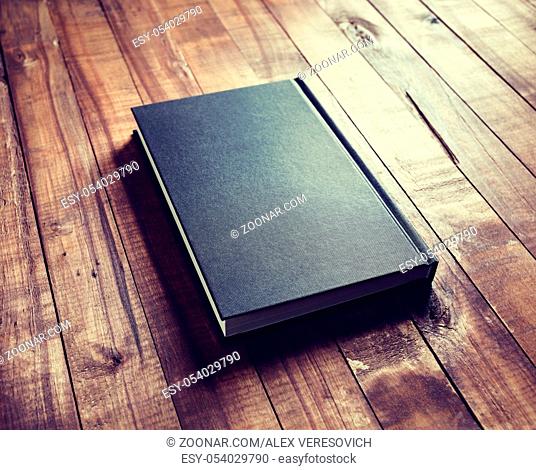 Blank black book cover on vintage wood table background. Vintage toned image